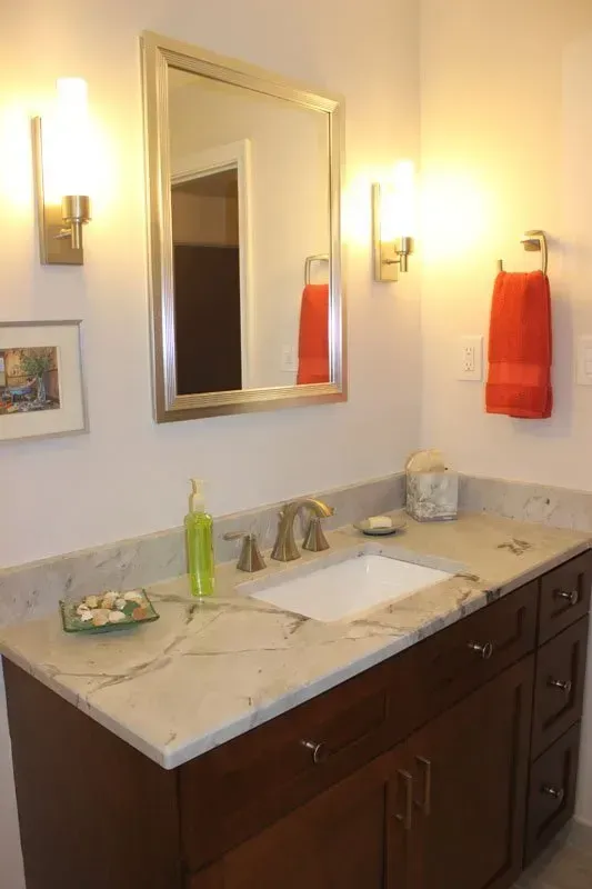 Modern bathroom vanity with marble countertop, mirror, wall sconces, and red towels In Bucks County PA