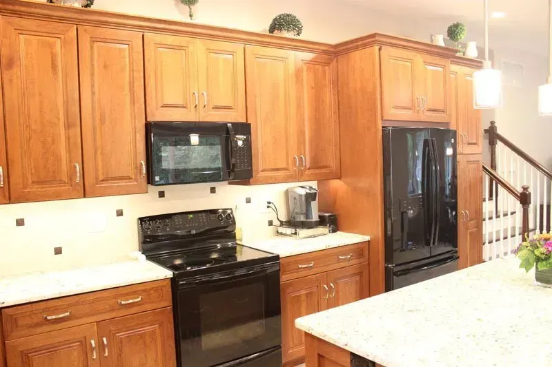 Bright kitchen with wooden cabinets, black appliances, white countertops, and a staircase in the background In Bucks County PA