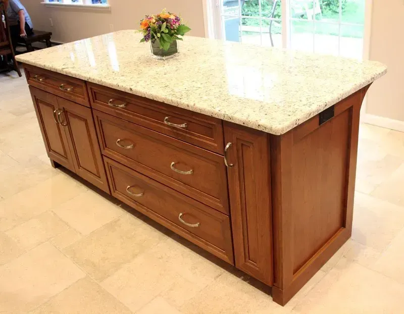 Wooden kitchen island with granite countertop and drawers, topped with a small flower arrangement. In Bucks County PA