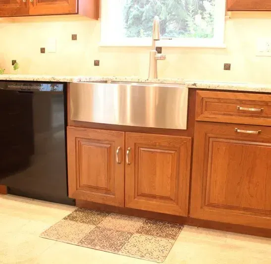 Kitchen with stainless farmhouse sink, wooden cabinets, black dishwasher, and window above the counter In Bucks County PA