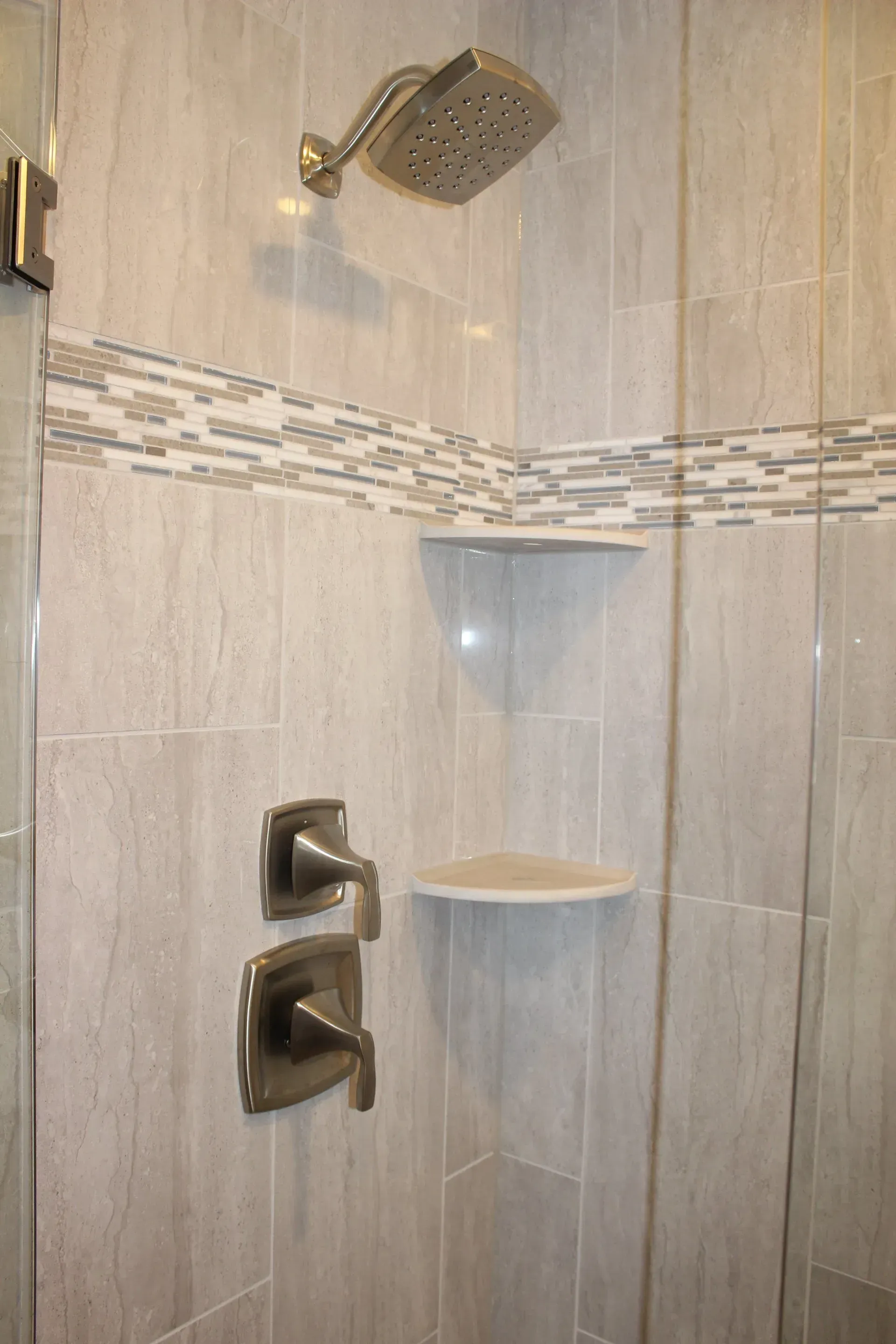 Walk-in shower with chrome fixtures, corner shelves, and beige tiled walls In Bucks County PA