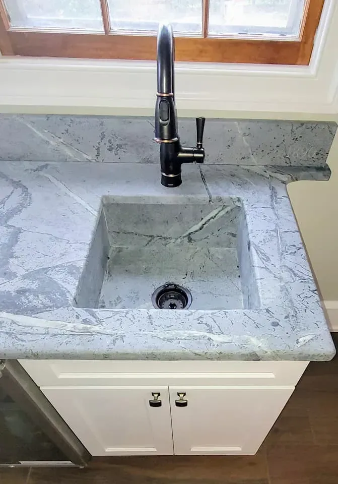 Kitchen sink with gray marble countertop, black faucet, and white cabinet below a window In Bucks County PA