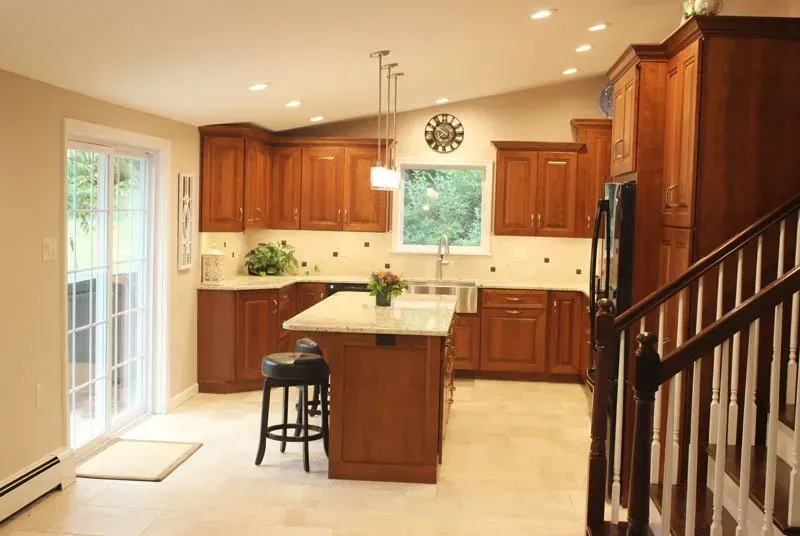 Bright kitchen with wood cabinets, central island, and staircase railing in the foreground In Bucks County PA