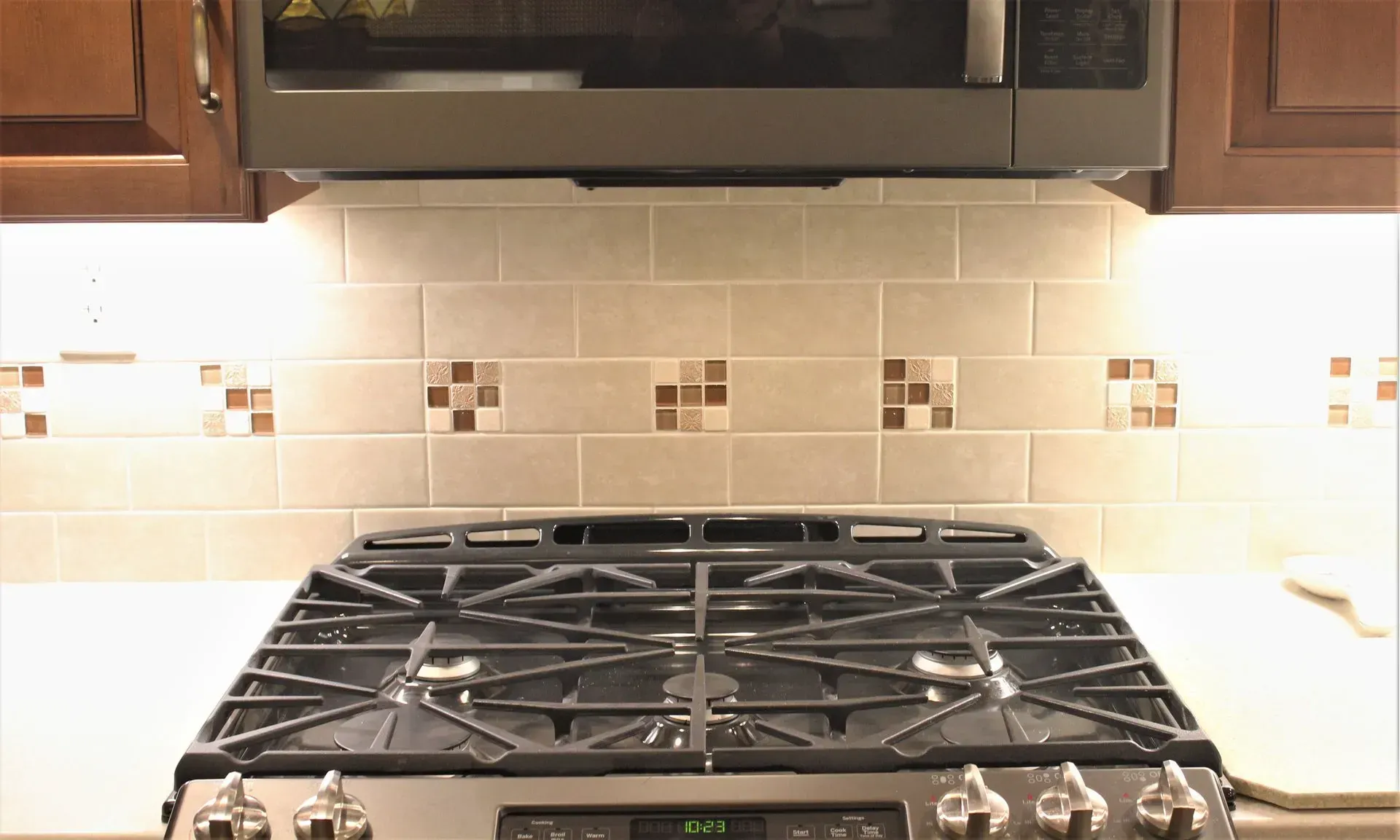 Kitchen stove with stainless steel gas burners beneath a black range hood and beige tile backsplash In Bucks County PA