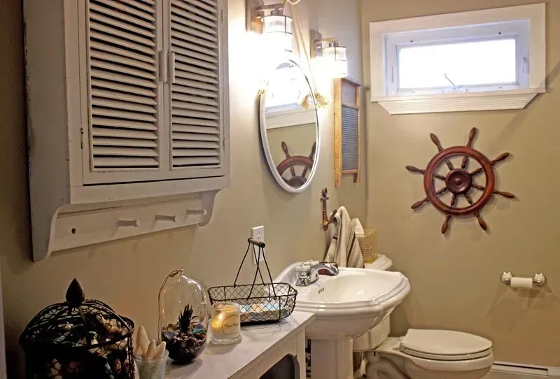 Small nautical-themed bathroom with sink, toilet, window, mirror, and ship wheel wall decor In Bucks Country PA