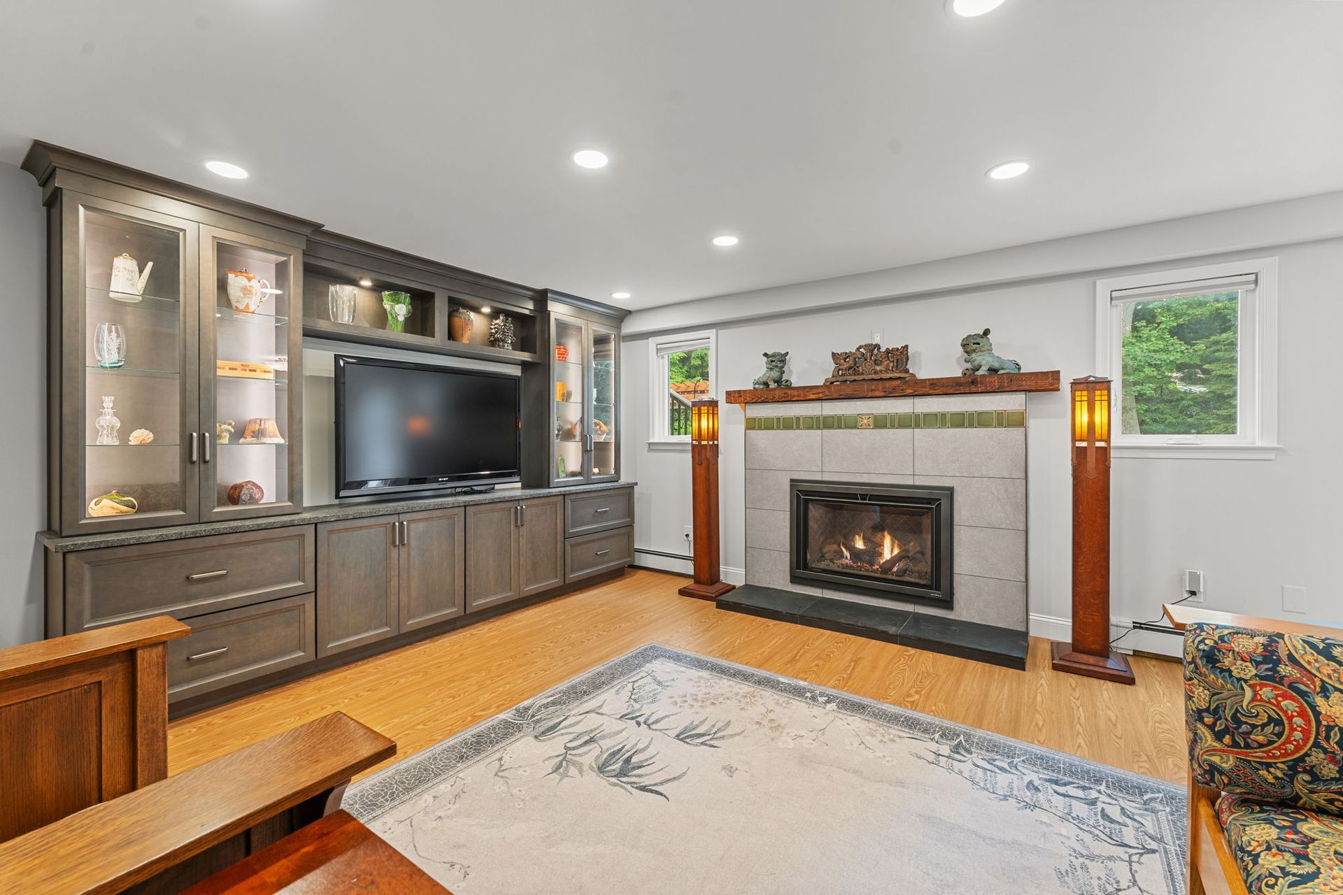Living room with built-in cabinets, fireplace, TV, and large window, in warm neutral tones  In Bucks County PA