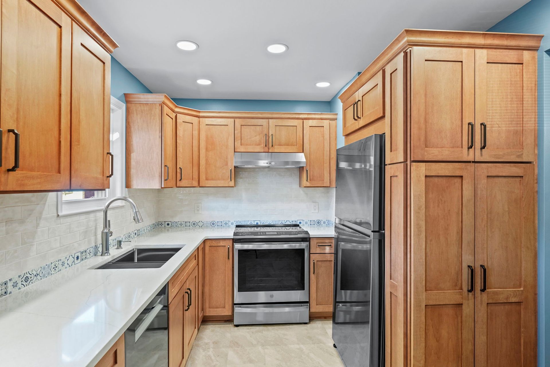 Bright modern kitchen with wood cabinets, white countertops, stainless appliances, and blue ceiling accents In Bucks County PA