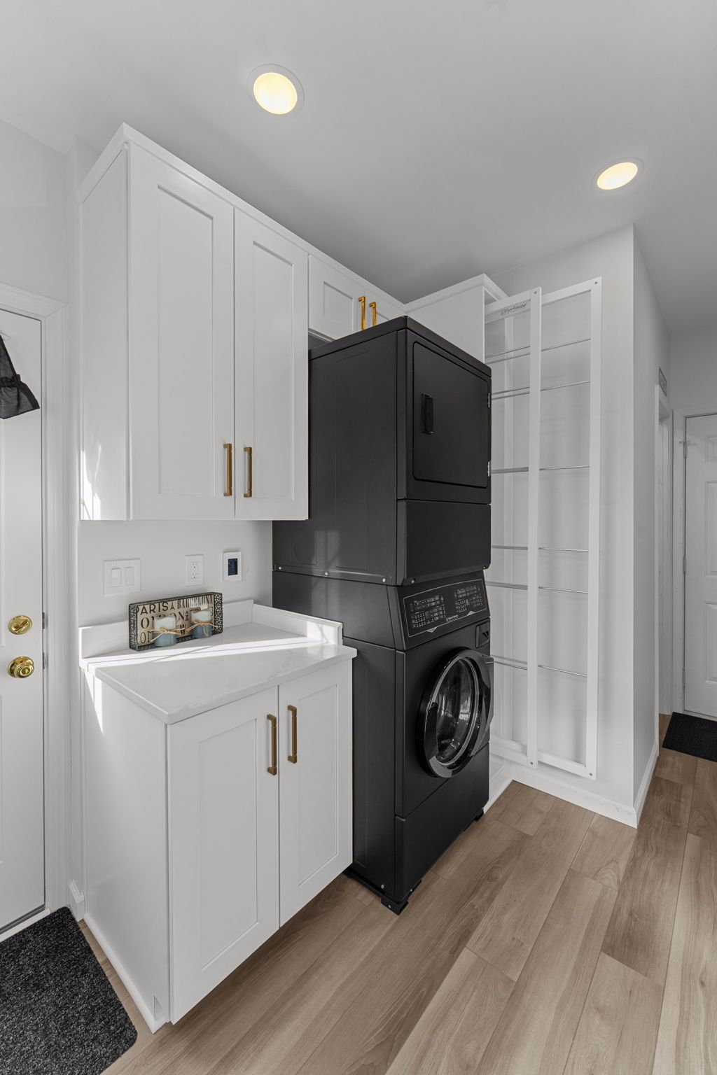 Small laundry nook with white cabinets, black washer-dryer stack, and light wood flooring In Bucks County PA