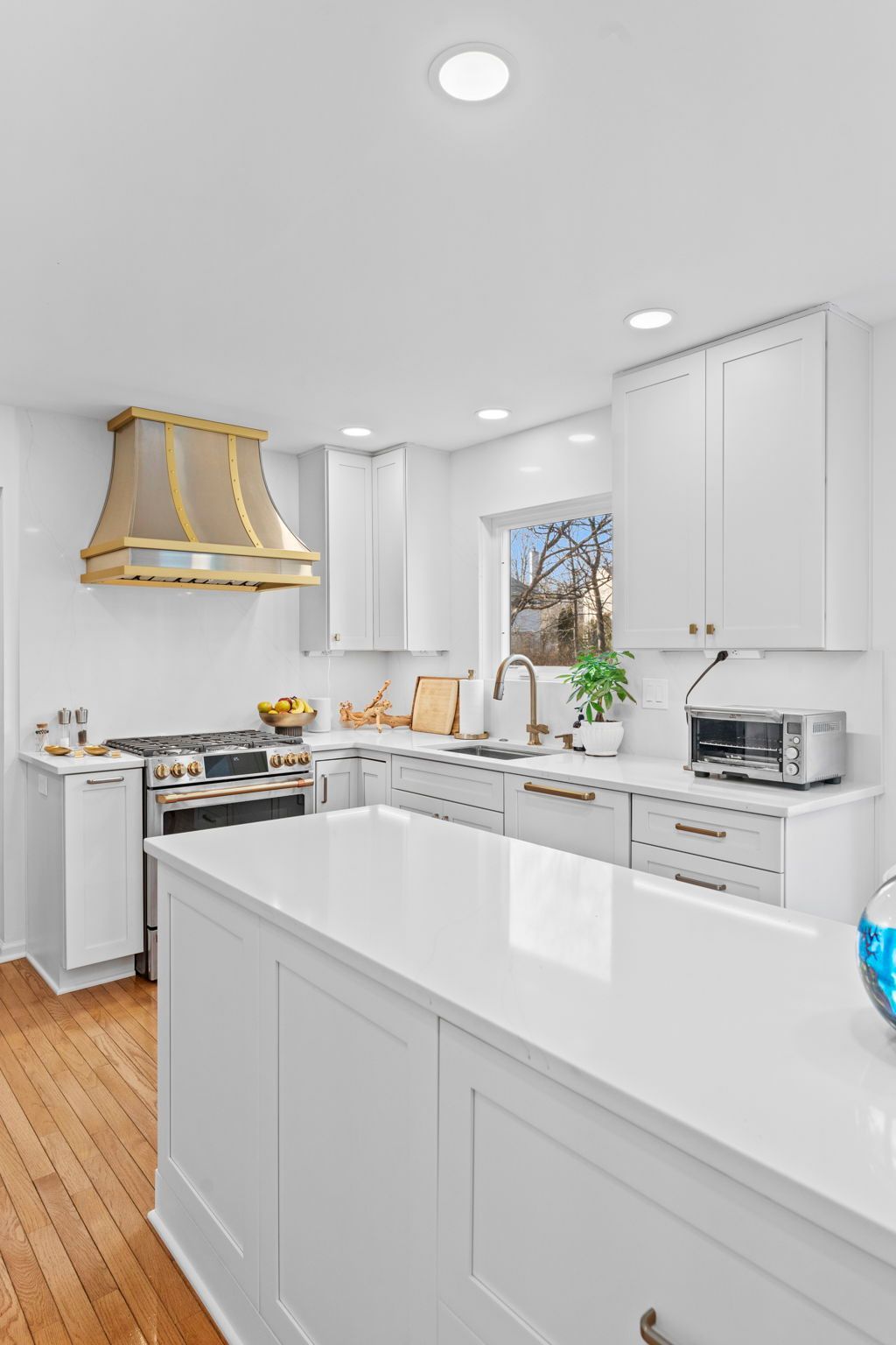 Bright white modern kitchen with island, gold range hood, marble counters, and wood floor In Bucks Country PA