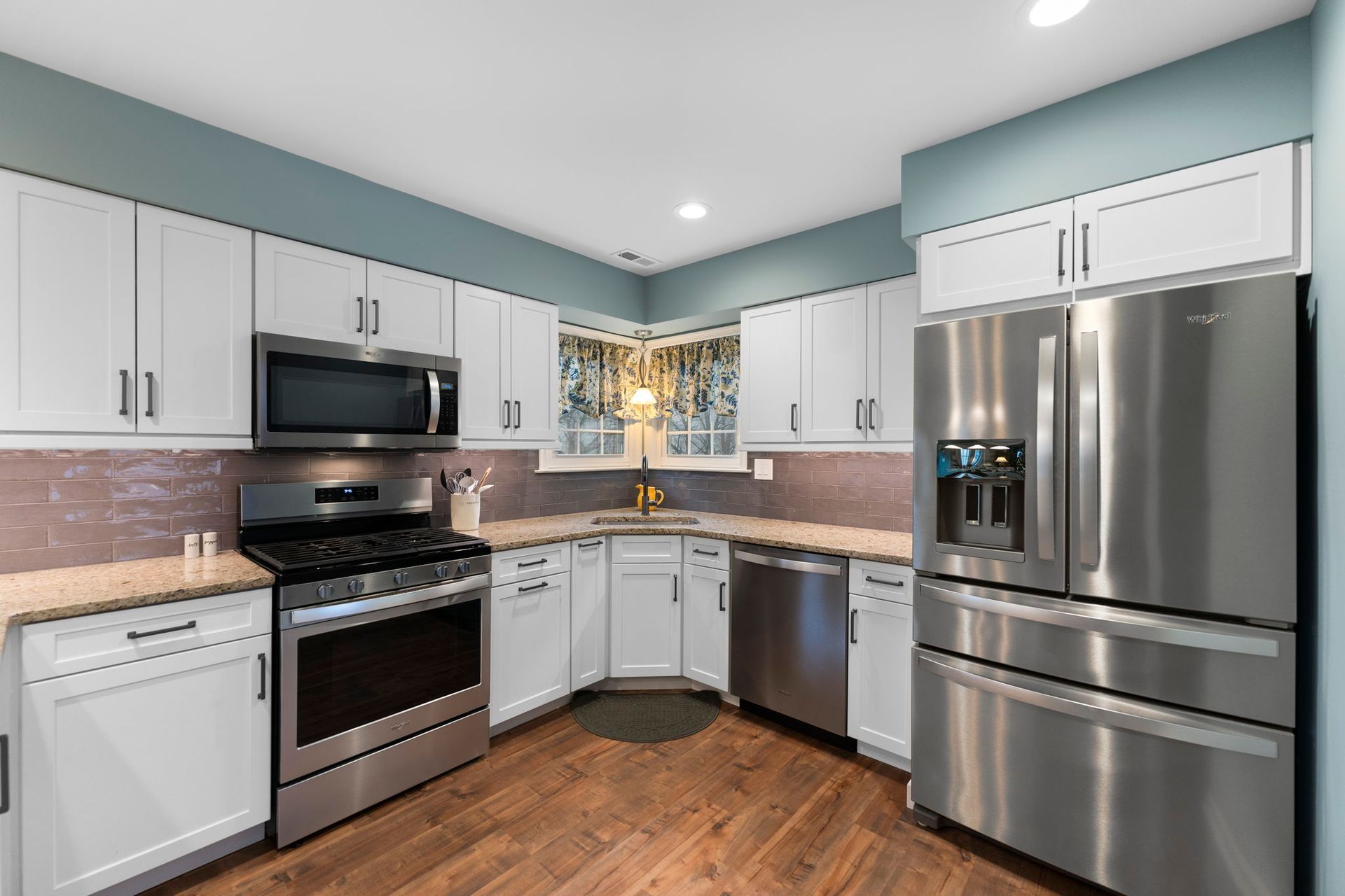 Modern kitchen with white cabinets, stainless appliances, light blue walls, and wood flooring In Bucks Country PA