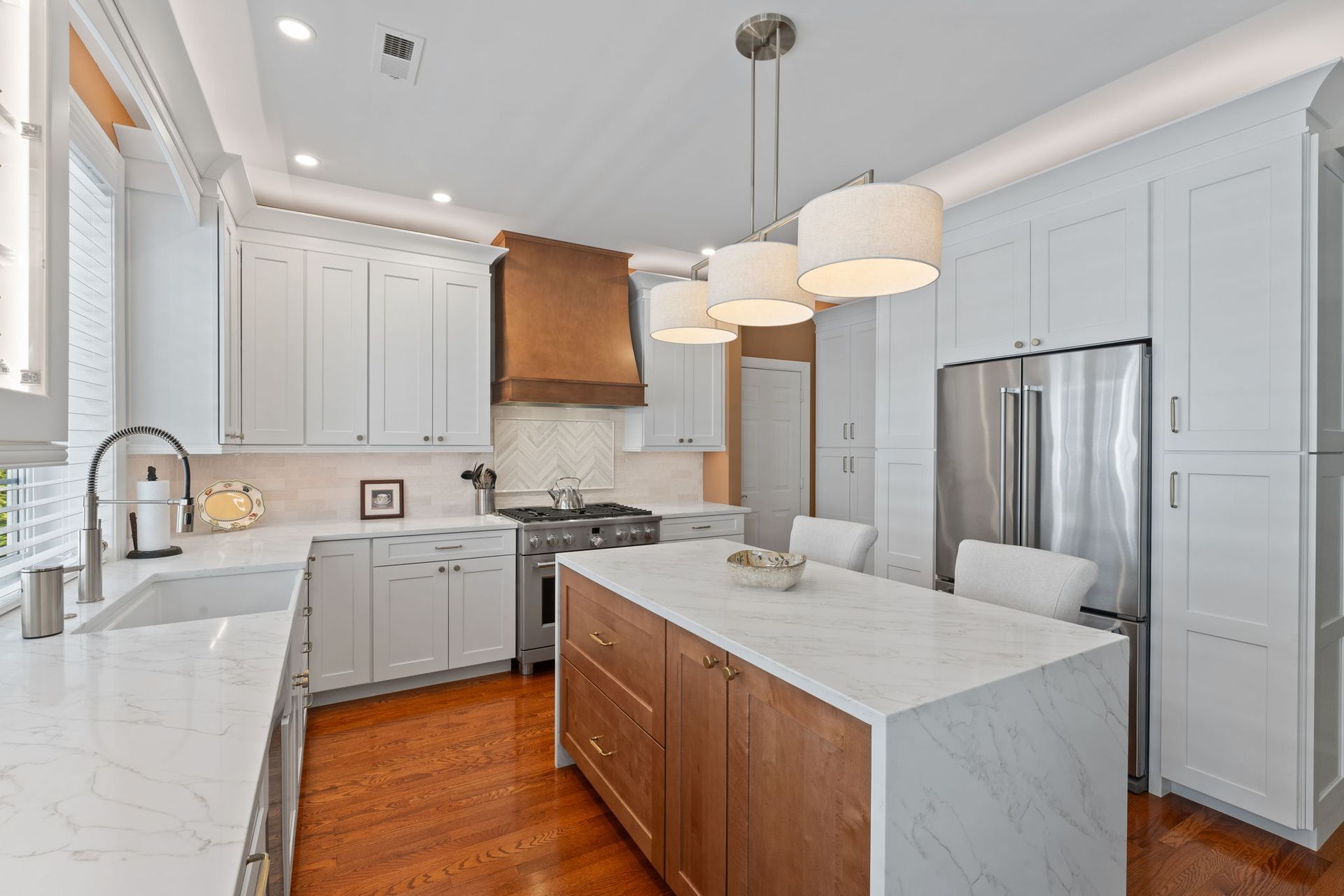 Bright modern kitchen with white cabinets, marble island, stainless fridge, and warm wood flooring In Bucks County PA