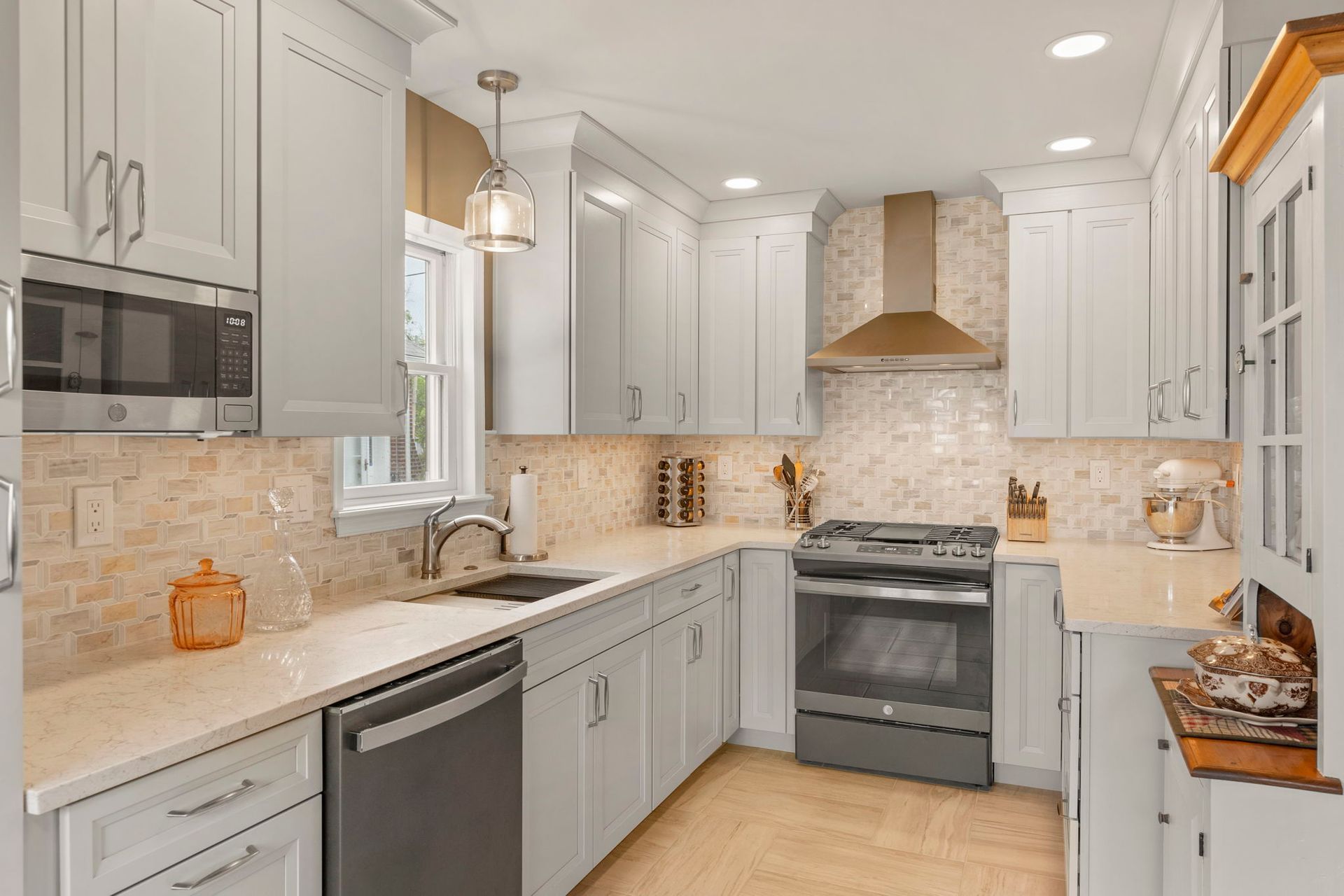 Bright modern kitchen with white cabinets, marble counters, stainless appliances, and beige tile backsplash In Bucks County PA