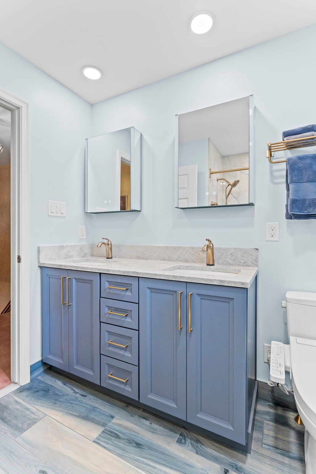 Blue bathroom vanity with marble countertop, gold faucets, and two mirrors in a bright, tiled room In Bucks County PA