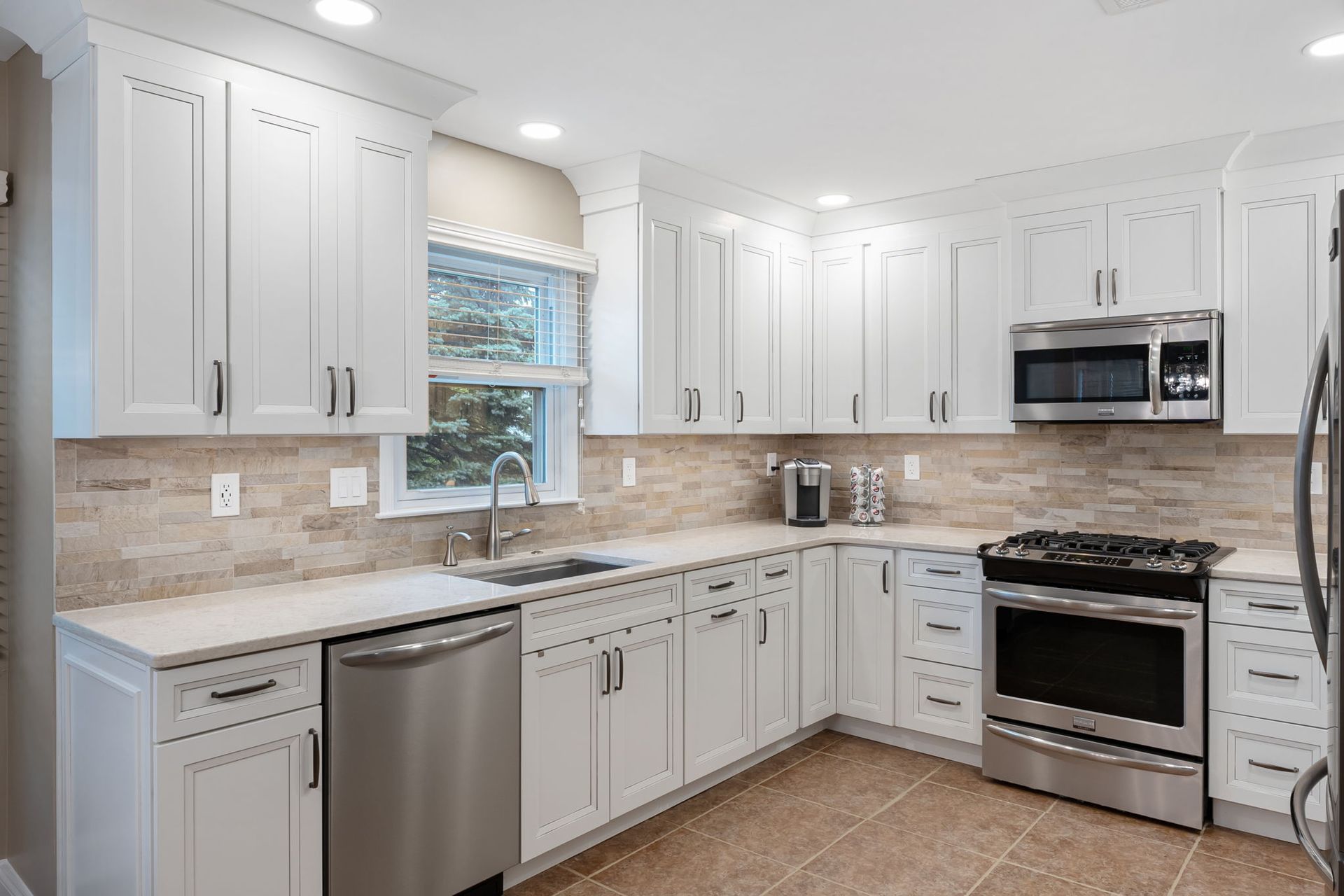 Bright white kitchen with stainless steel appliances, gray cabinets, and a window over the sink In Bucks Country PA