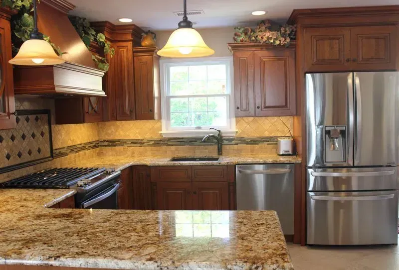 Modern kitchen with wood cabinets, granite counters, stainless steel fridge, and a window above the sink  In Bucks County PA