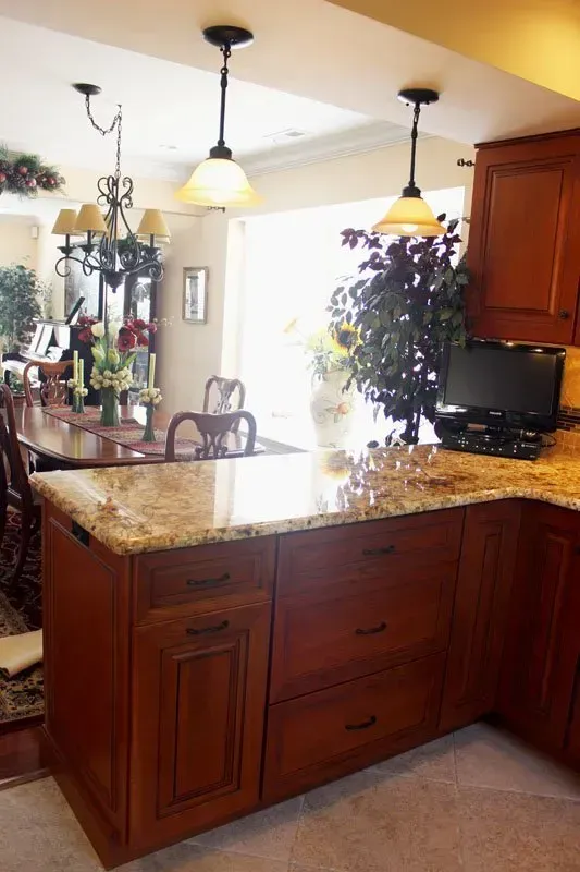 Kitchen with granite island, hanging pendant lights, and warm wood cabinets near a bright dining area  In Bucks County PA