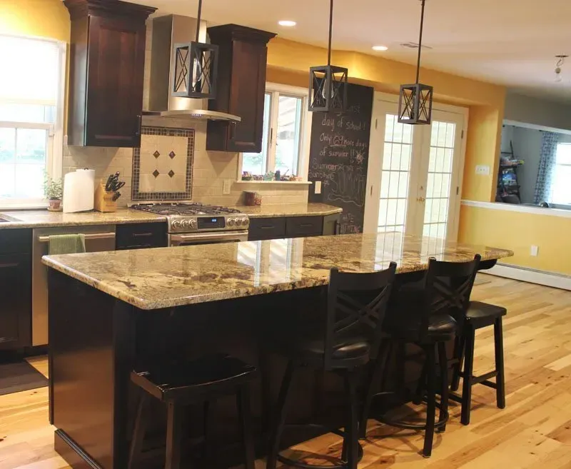 Modern kitchen with granite island, dark stools, pendant lights, and hardwood floors In Bucks County PA