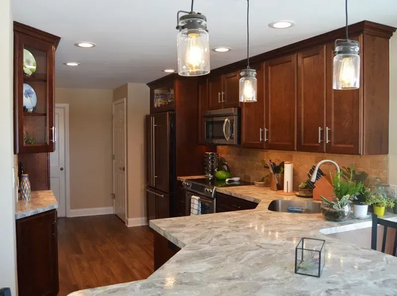 Modern kitchen with dark wood cabinets, marble countertop, stainless appliances, and hanging pendant lights In Bucks Country PA