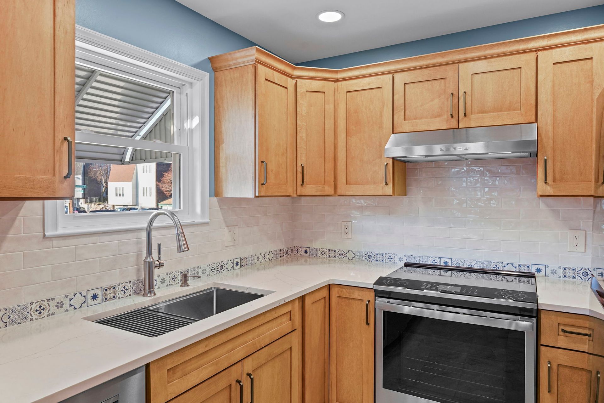 Kitchen with light wood cabinets, stainless steel sink, and stove under a range hood In Bucks County PA