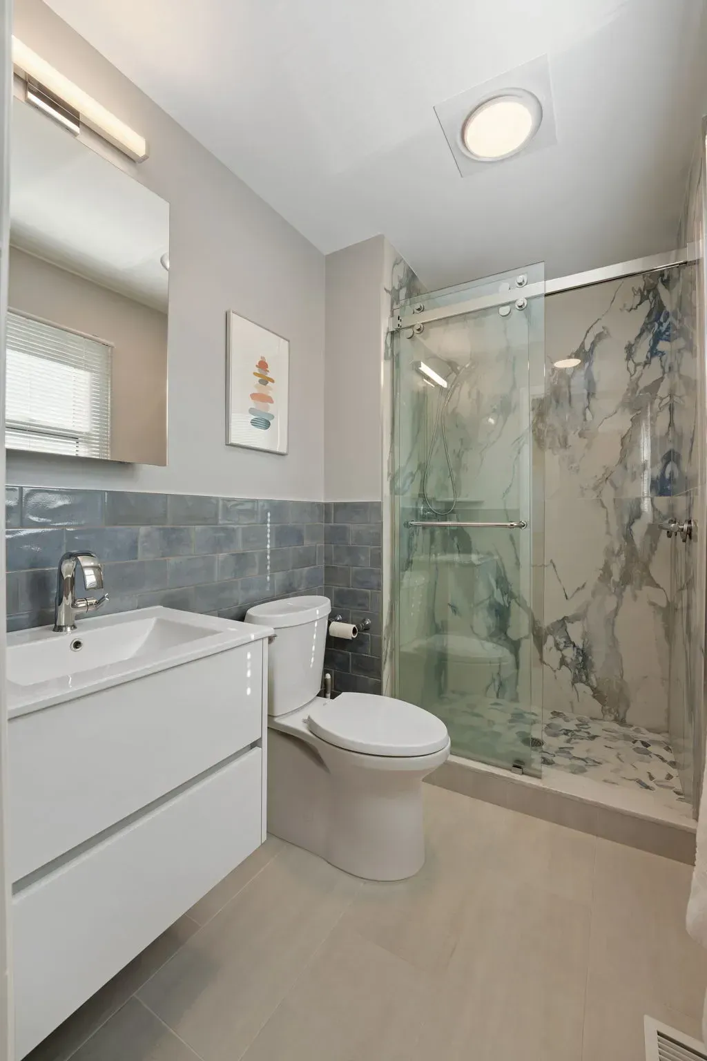 Modern bathroom with vanity, toilet, glass shower, and gray-blue tiled walls  In Bucks County PA