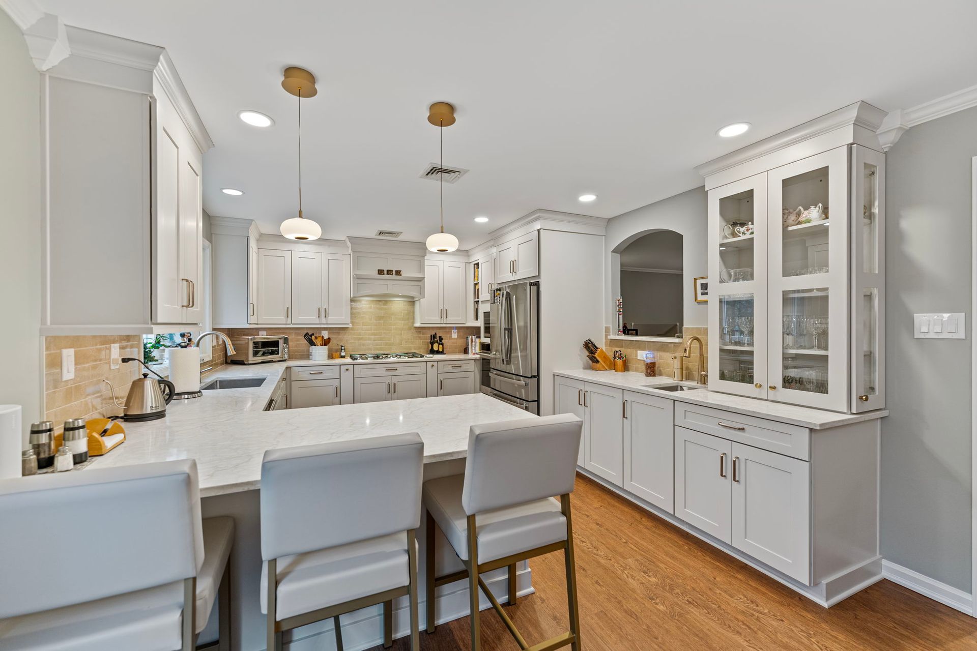 Bright white kitchen and dining area with island, bar stools, cabinet display, and hardwood floors In Bucks County PA