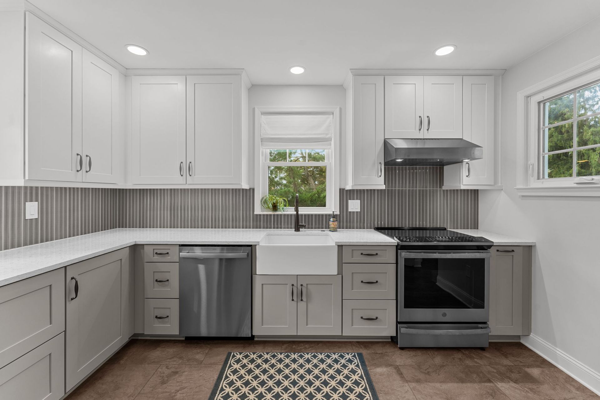 Bright white kitchen with gray cabinets, stainless appliances, window, and patterned rug In Bucks Country PA