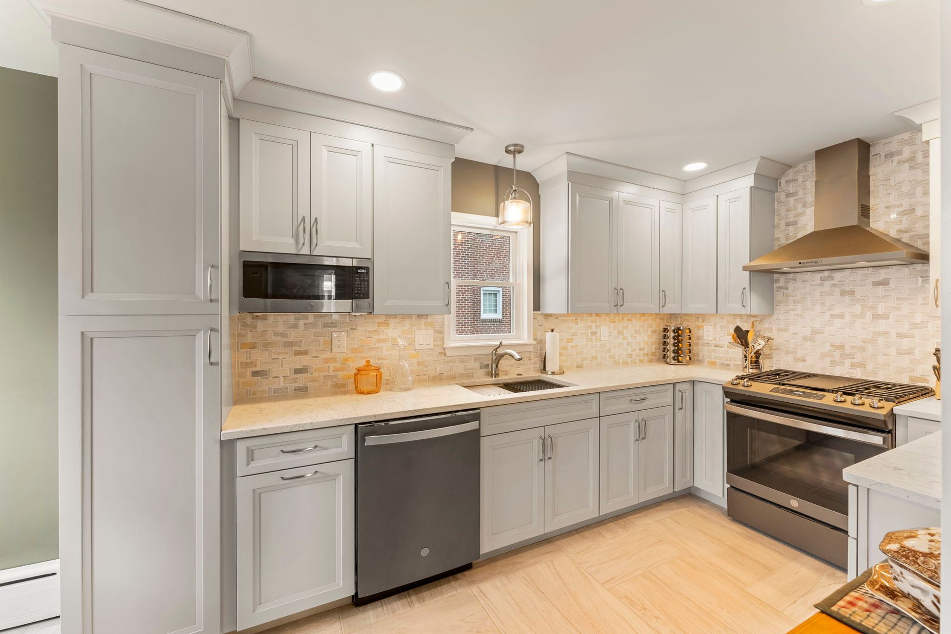 Bright modern kitchen with white cabinets, gray lower cabinets, stainless appliances, and beige tile backsplash In Bucks County PA