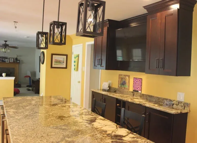 Modern kitchen with granite counters, dark wood cabinets, pendant lights, and a wall-mounted TV In Bucks County PA