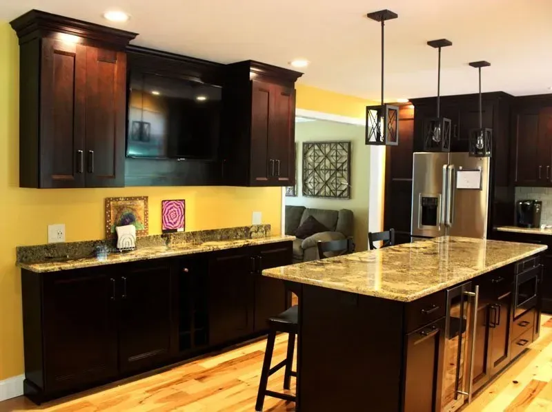 Modern kitchen with dark wood cabinets, granite island, and stainless steel appliances under pendant lights In Bucks County PA