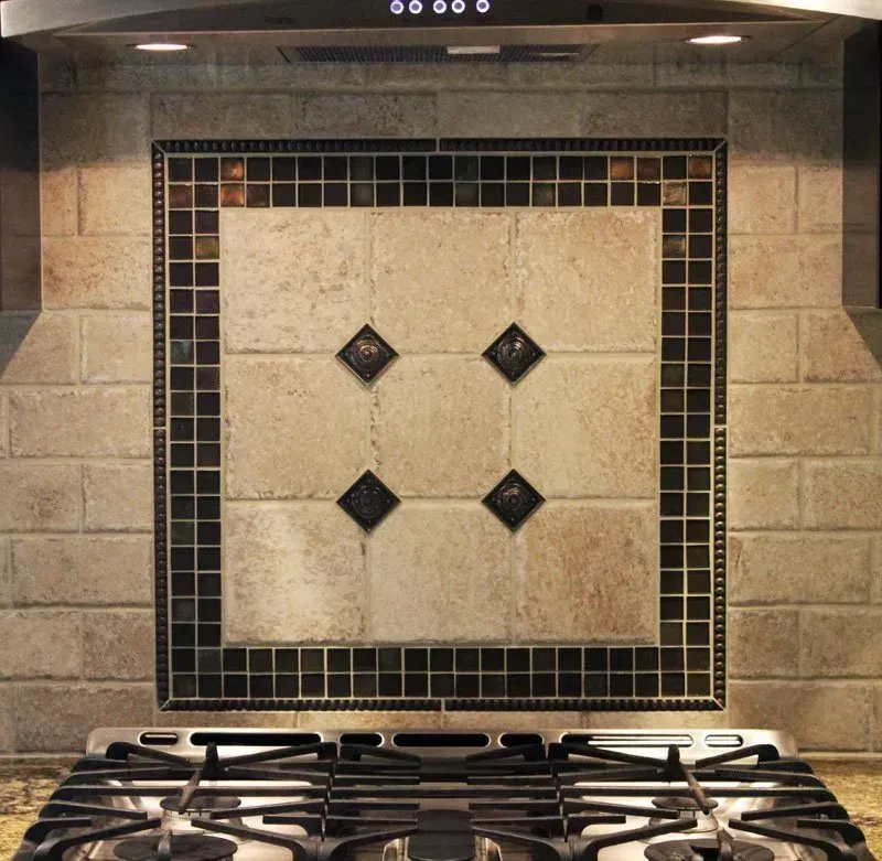 Kitchen stove backsplash with beige stone tiles and dark mosaic border above burners In Bucks County PA