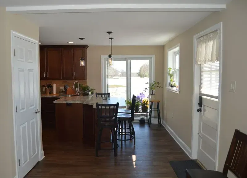 Bright kitchen and dining area with wooden floors, bar stools, and a sliding glass door to the outside In Bucks County PA