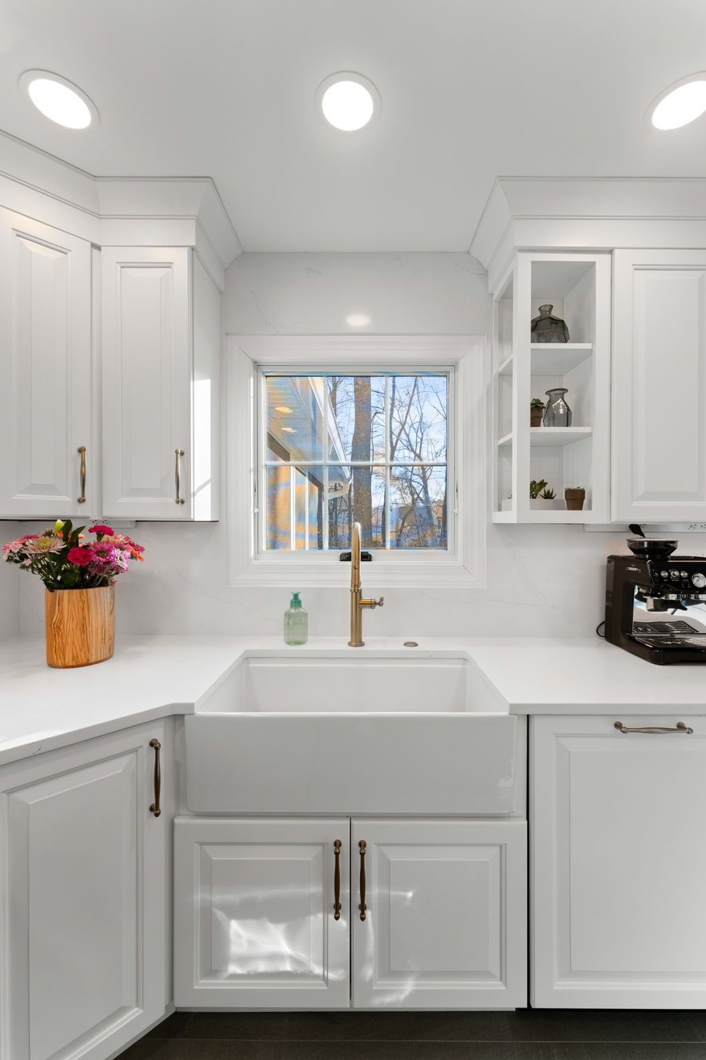 Bright white kitchen with farmhouse sink, gold faucet, window, and recessed ceiling lights In Bucks Country PA
