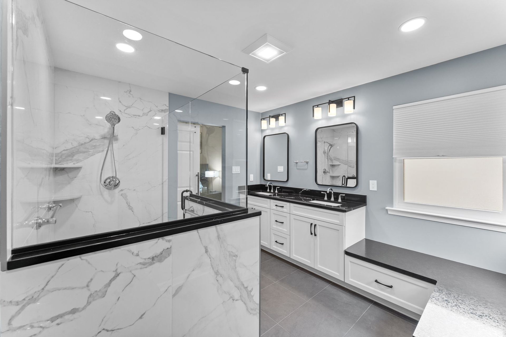 Modern gray-and-white bathroom with marble shower, double vanity, and large window seat In Bucks County PA