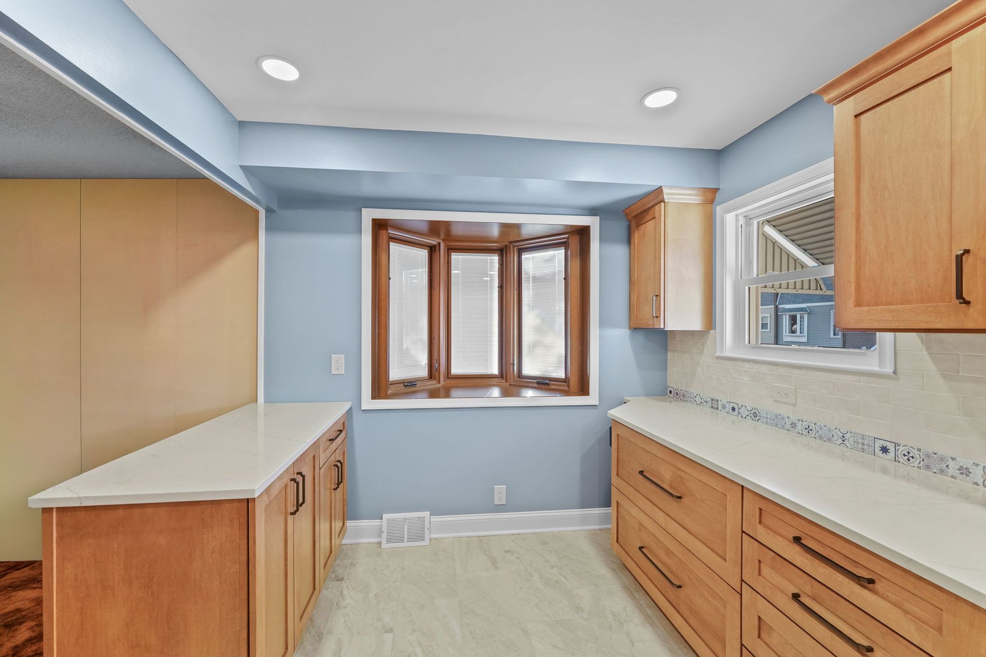 Empty kitchen with light blue walls, wood cabinets, white countertops, and a bay window In Bucks County PA
