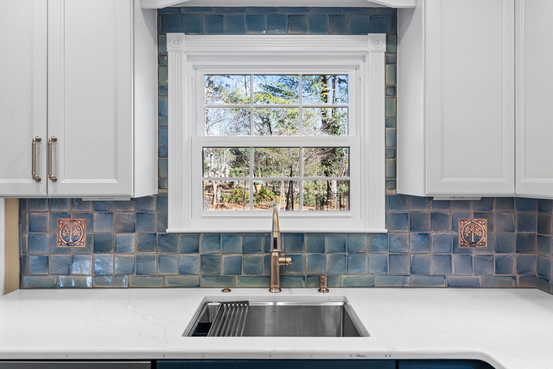 Bright kitchen sink under a window, with white cabinets and blue tile backsplash  In Bucks County PA