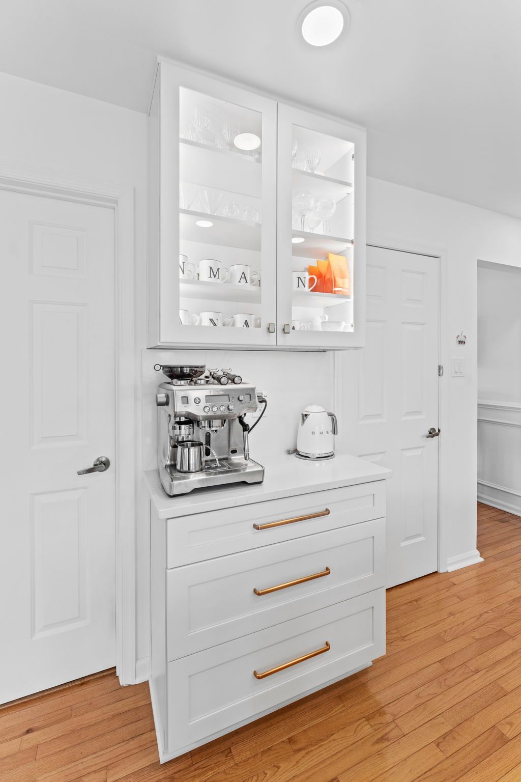 White kitchen cabinet with glass doors, coffee maker, toaster, and drawers against hardwood floors In Bucks Country PA