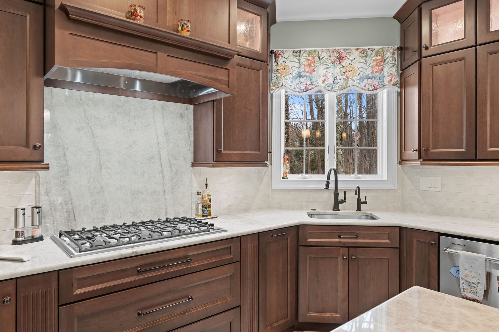 Modern kitchen with dark wood cabinets, white countertops, gas range, and window over the sink In Bucks Country PA