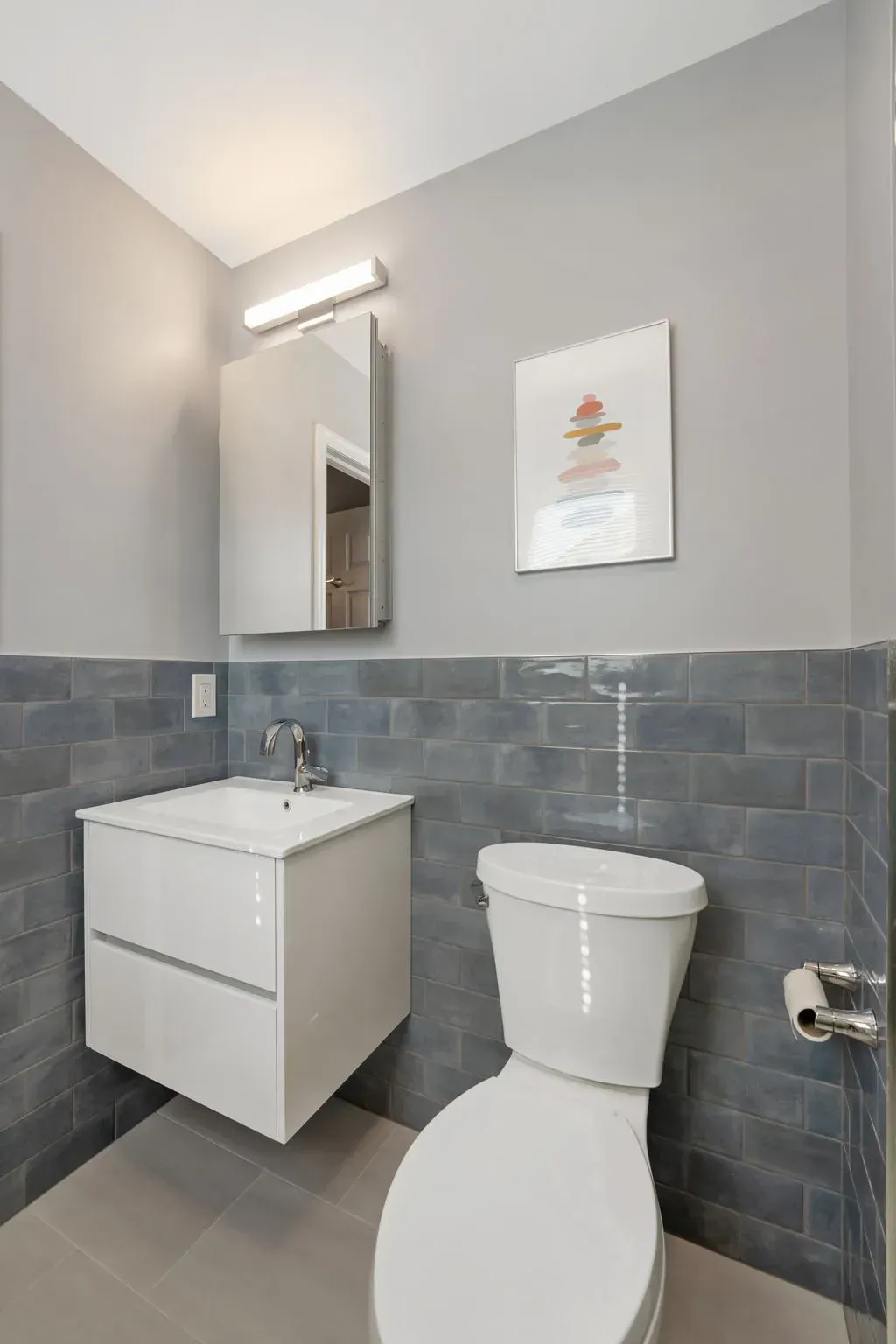 Modern bathroom with white vanity, mirror, toilet, and gray tile walls  In Bucks County PA