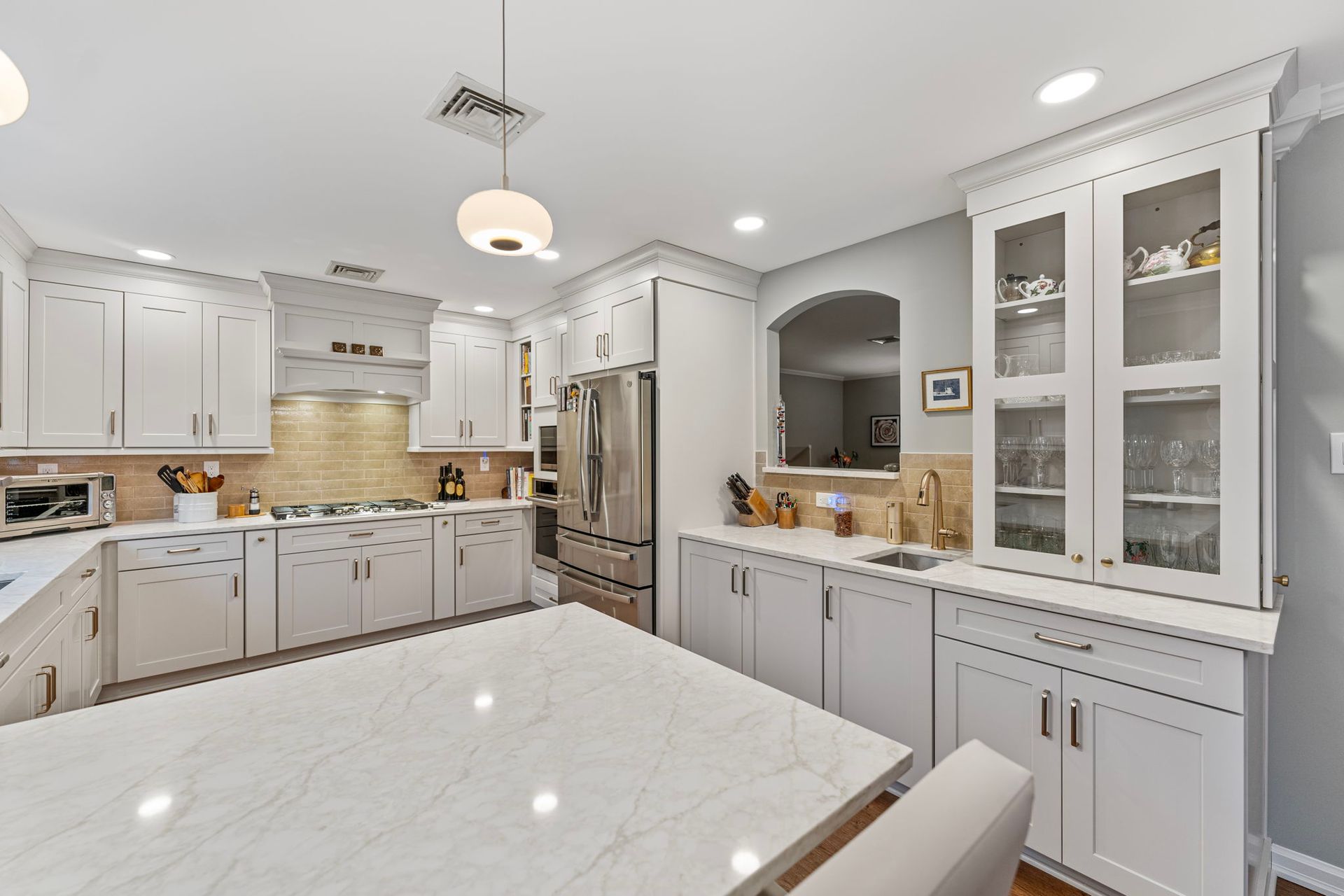 Bright white modern kitchen with marble island, stainless appliances, and glass-front cabinets In Bucks County PA