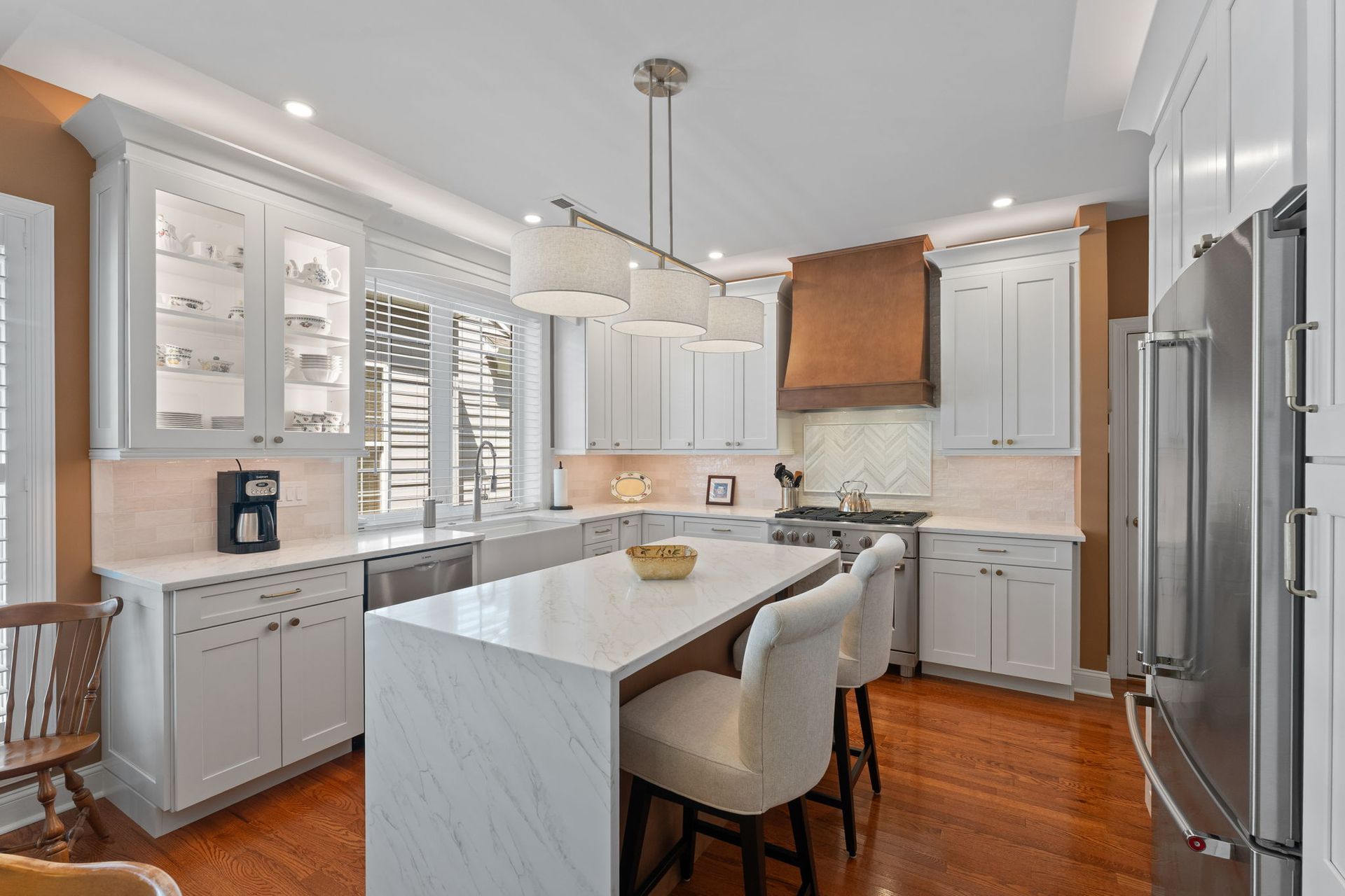 Bright modern kitchen with white cabinets, marble island, stainless steel appliances, and wood floors In Bucks County PA