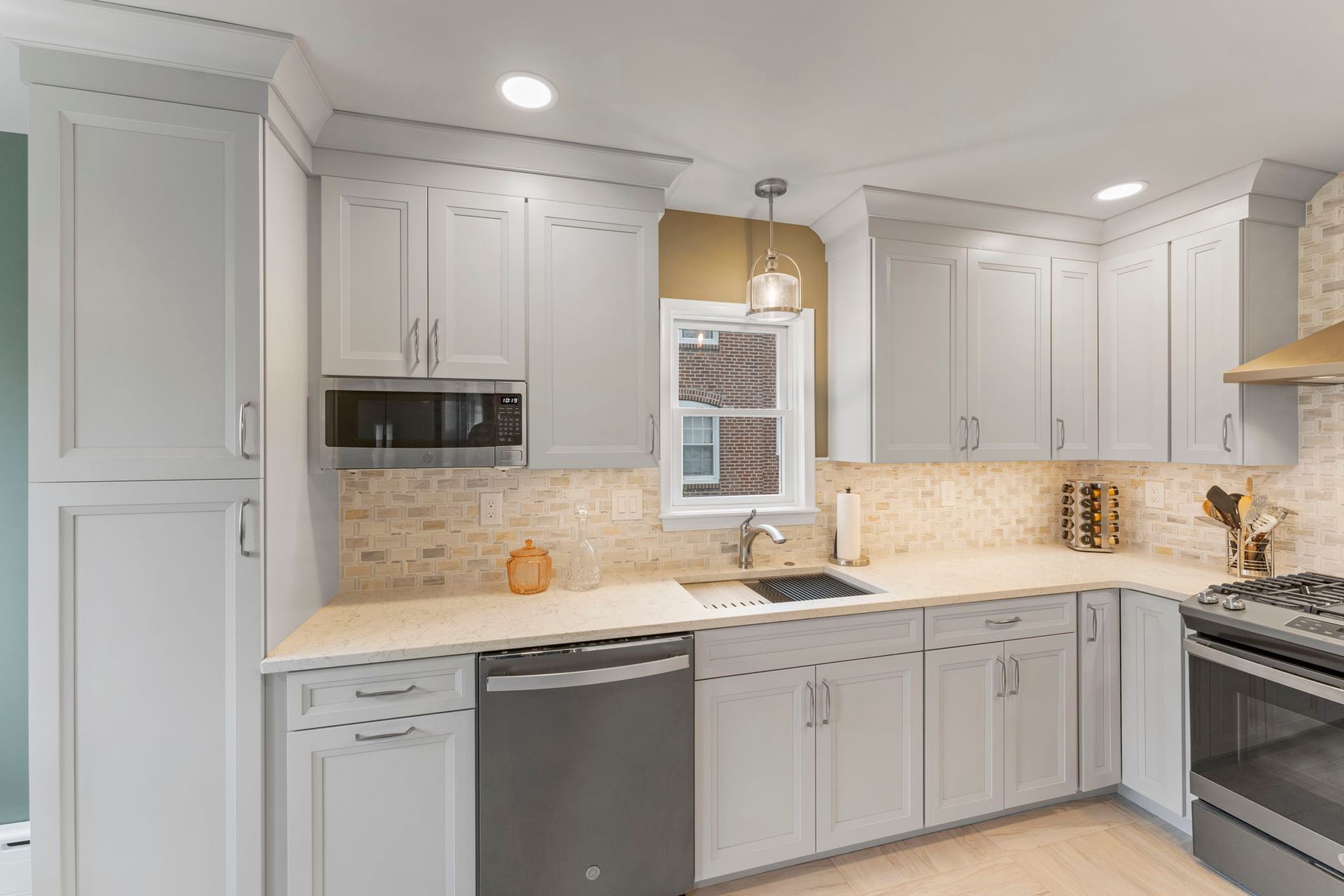 Bright modern kitchen with white cabinets, stainless appliances, beige countertops, and tiled backsplash In Bucks County PA