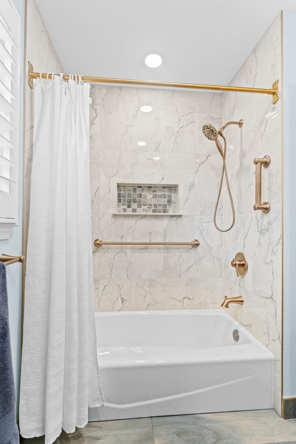 White marble bathroom with gold fixtures, a shower curtain, and a built-in tub-shower combo In Bucks County PA