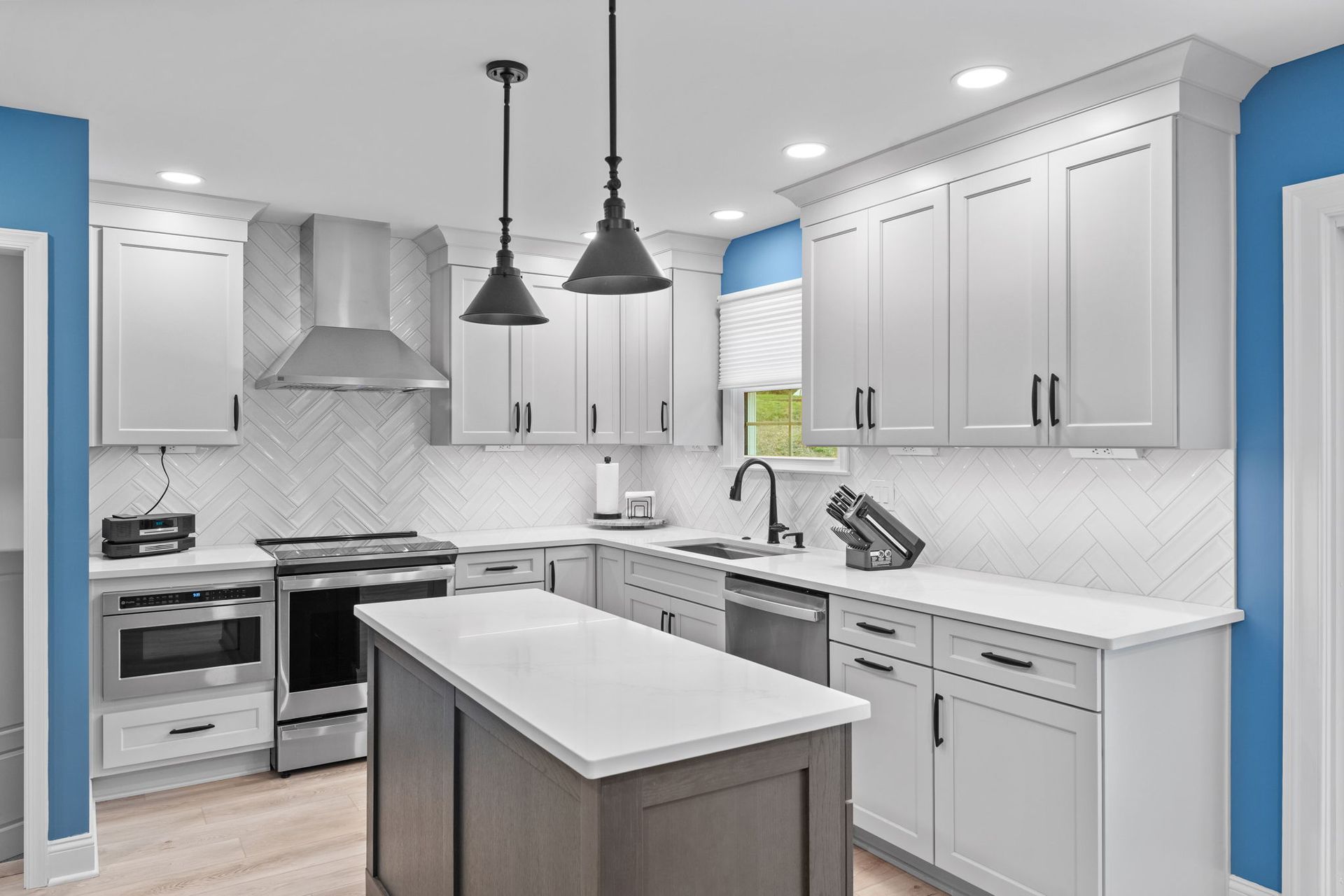 Bright modern white kitchen with island, stainless appliances, pendant lights, and blue accent walls in Bucks County PA