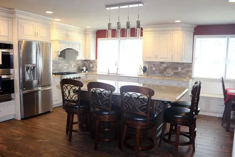 Bright kitchen with stainless steel appliances, white cabinets, center island, and dark wooden chairs and table  In Bucks County PA