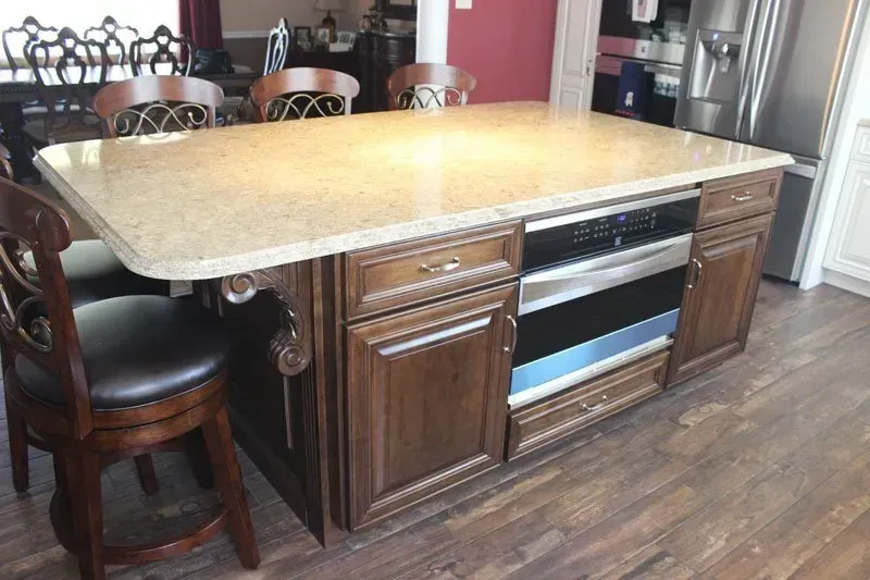 Kitchen island with beige countertop, built-in oven, and dark wood cabinets in a home kitchen  In Bucks County PA
