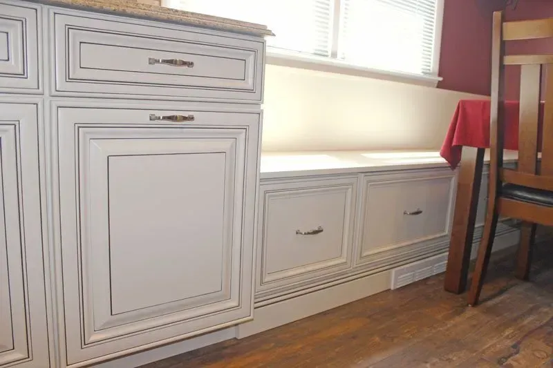 Built-in white cabinets with drawers under a window beside a wooden table and chair, on a hardwood floor  In Bucks County PA