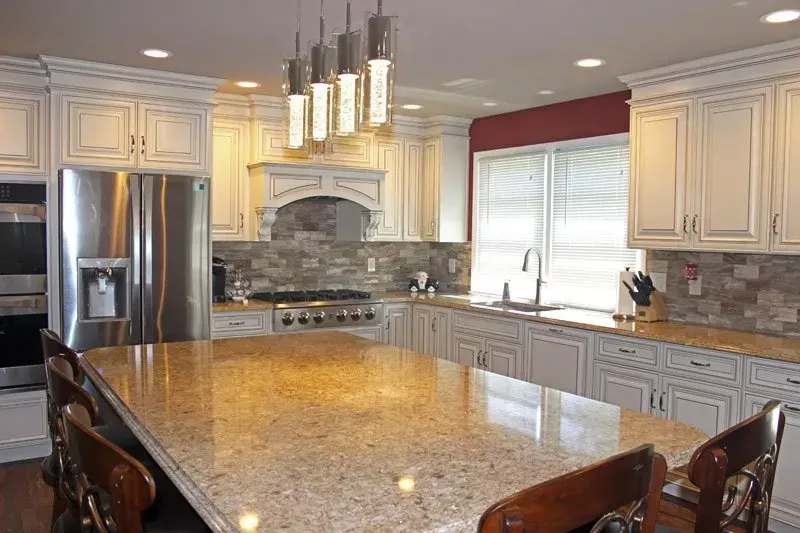 Bright modern kitchen with white cabinets, granite island, stainless steel fridge, and stone backsplash  In Bucks County PA