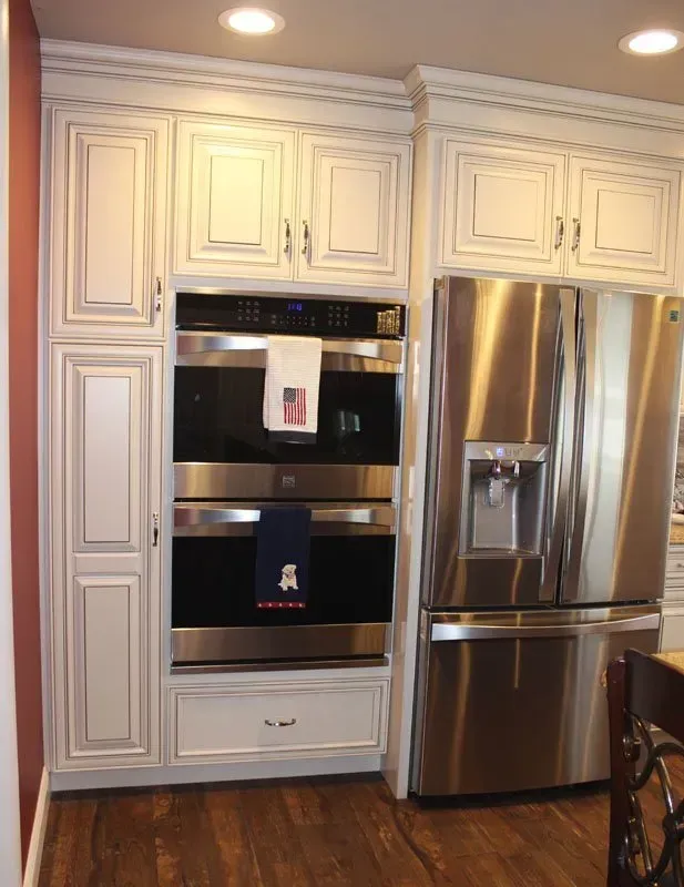 Built-in stainless steel oven beside a stainless refrigerator in a white kitchen with cabinetry  In Bucks County PA