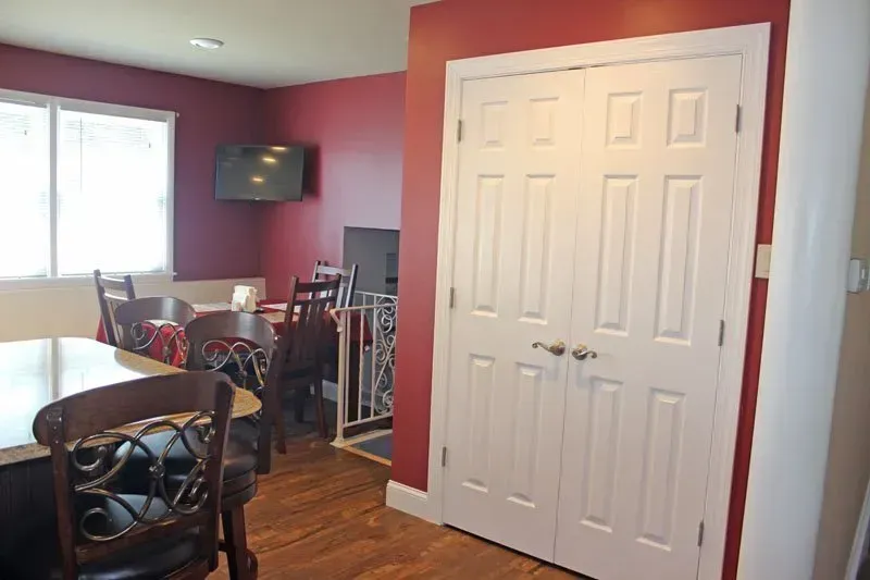 Dining room with red walls, white closet doors, wooden table, chairs, and a wall-mounted TV ליד window  In Bucks County PA