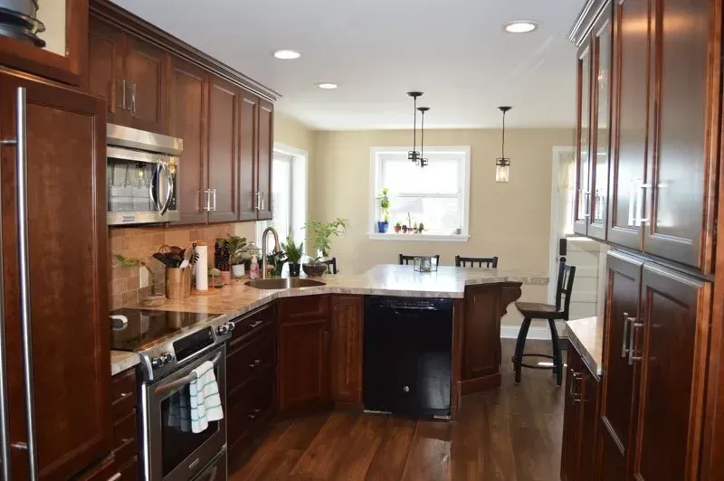 Modern kitchen with dark wood cabinets, black countertops, stainless appliances, and a breakfast nook by the window In Bucks County PA